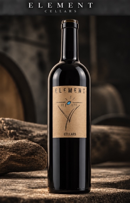 Tall Element Cellars Cabernet Sauvignon wine bottle with tan label and turquoise sun, photographed against oak barrels and rustic wood
